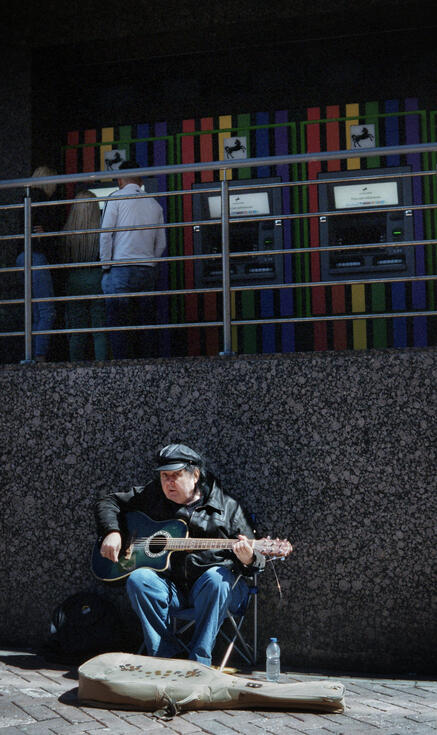 Busker playing guitar beneath a row of cash machines Busker playing guitar beneath a row of cash machines