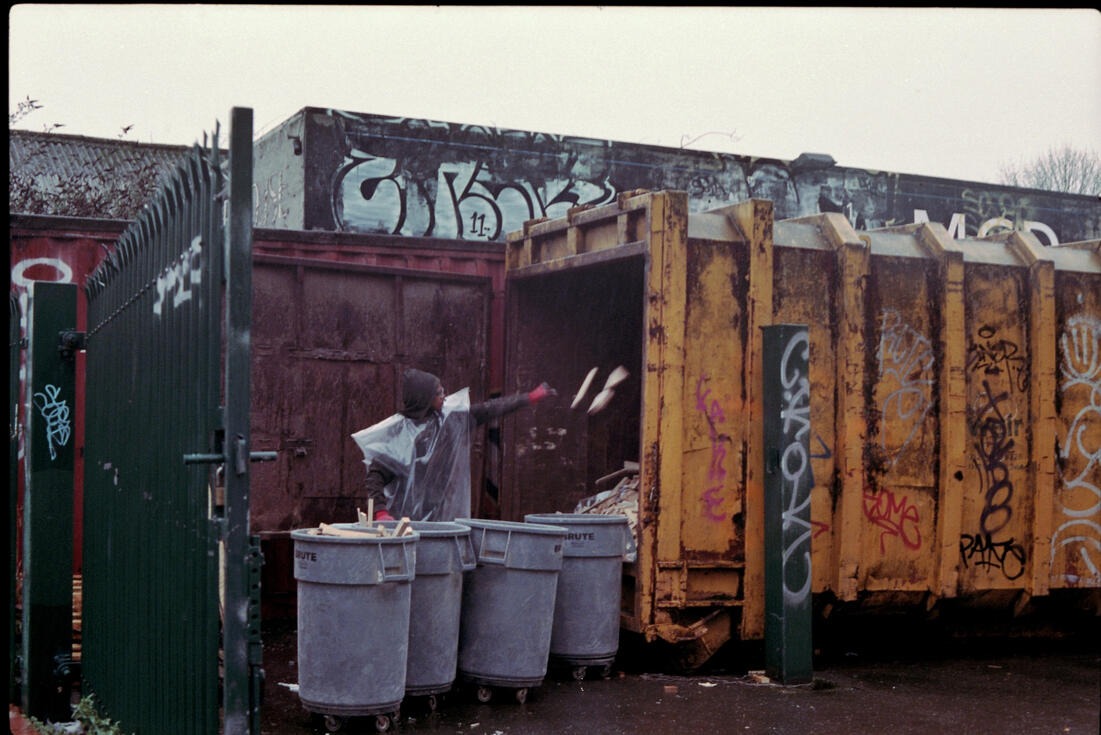 Man loading waste into a graffiti-covered skip Man loading waste into a graffiti-covered skip