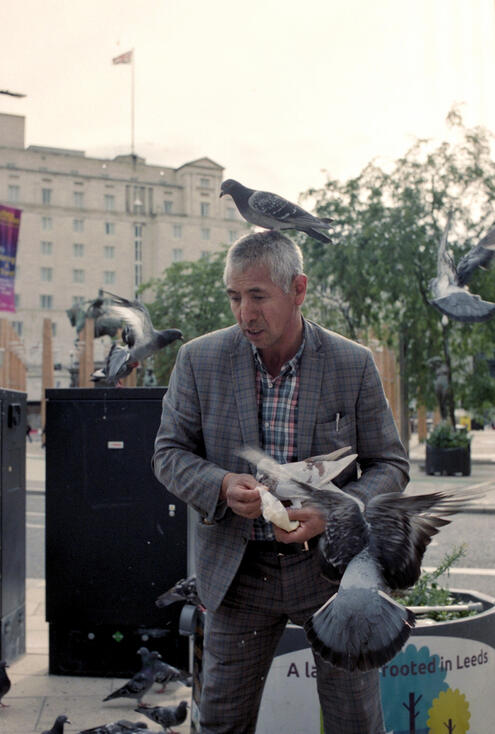 Man feeding pigeons that flock around him in Leeds Man feeding pigeons that flock around him in Leeds