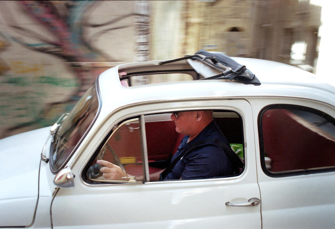 Man driving a classic Fiat 500 through town, Sardinia Man driving a classic Fiat 500 through town, Sardinia