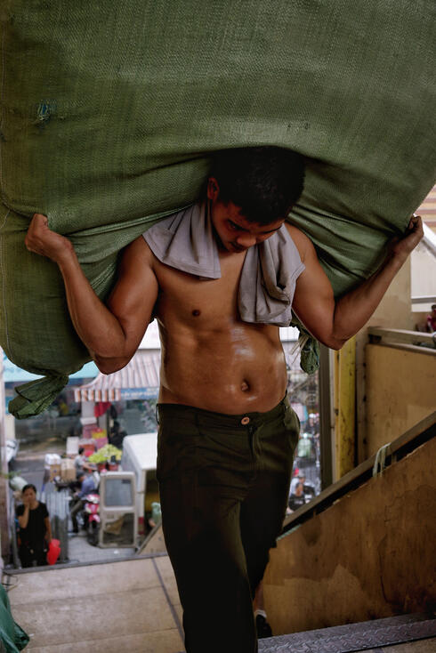 Shirtless porter carrying a heavy sack through a Hanoi market Shirtless porter carrying a heavy sack through a Hanoi market