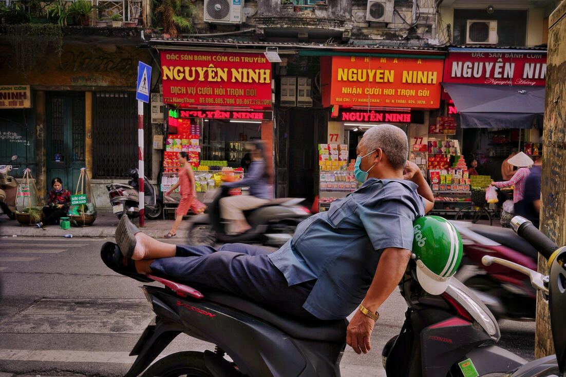 Man relaxing on his parked scooter outside Hanoi shops Man relaxing on his parked scooter outside Hanoi shops