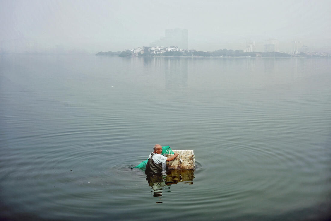 Man wading through misty West Lake at dawn, Hanoi Man wading through misty West Lake at dawn, Hanoi