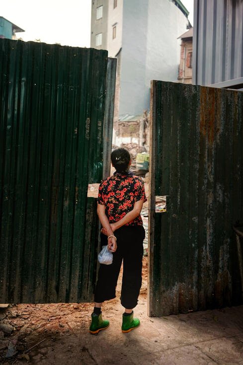Woman in a floral shirt beside a corrugated demolition gate, Hanoi Woman in a floral shirt beside a corrugated demolition gate, Hanoi