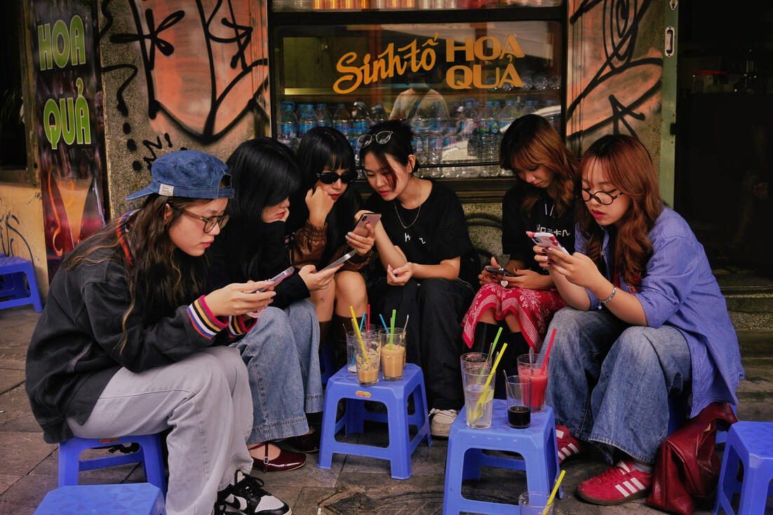 Young women on their phones at a Hanoi street smoothie bar Young women on their phones at a Hanoi street smoothie bar